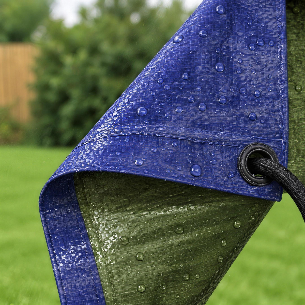 Close-up of the reversible tarpaulin corner: dark blue weave, olive green reverse, eyelet and bungee cord