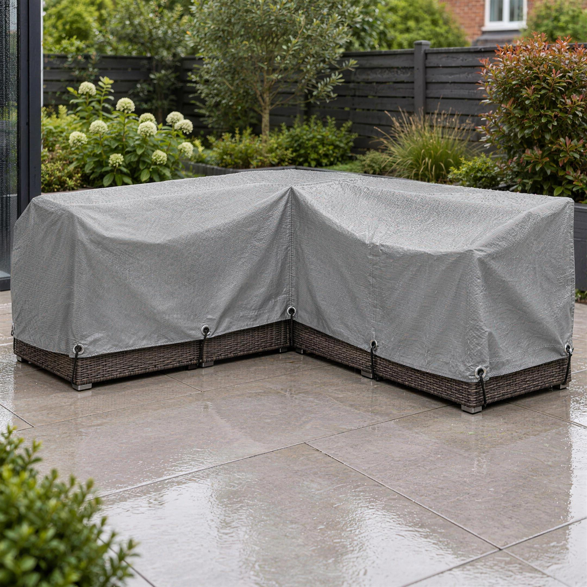 Light grey tarpaulin covering a rattan corner sofa on a modern patio in the rain